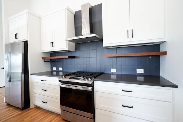 kitchen with white cabinets, stainless steel appliances, wall chimney range hood, and light hardwood / wood-style floors