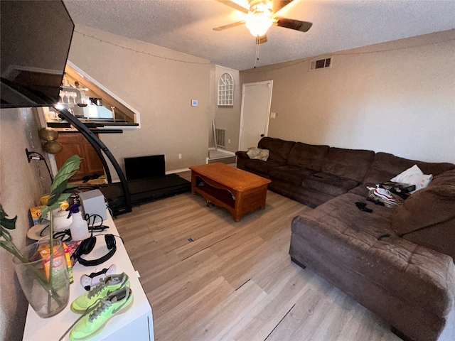 living room featuring ceiling fan, light wood-type flooring, and a textured ceiling