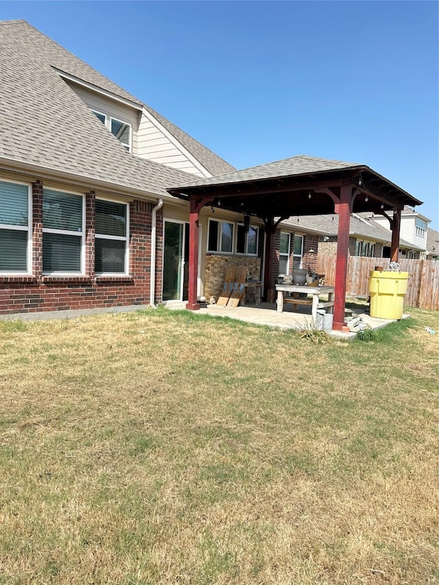 back of property featuring a lawn, fence, roof with shingles, and a patio area