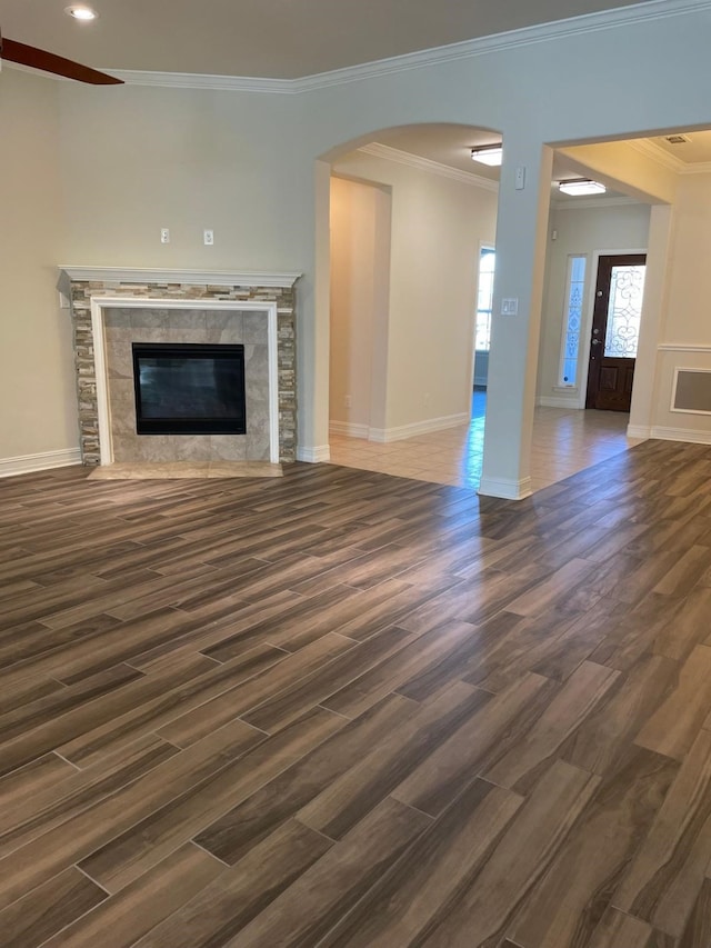 unfurnished living room featuring crown molding, a premium fireplace, arched walkways, baseboards, and wood finished floors