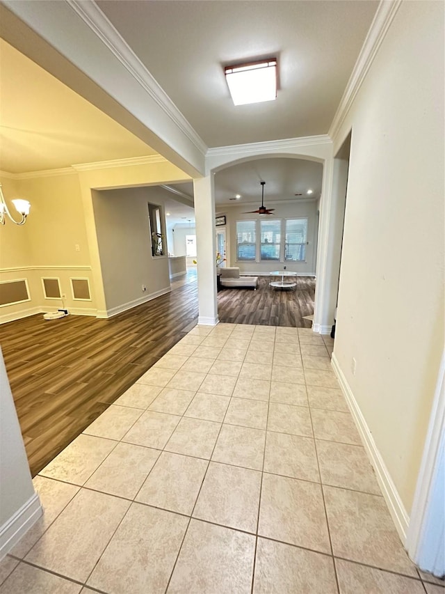 corridor with crown molding, tile patterned flooring, arched walkways, and an inviting chandelier