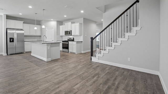 kitchen with light hardwood / wood-style flooring, an island with sink, white cabinets, decorative light fixtures, and stainless steel appliances