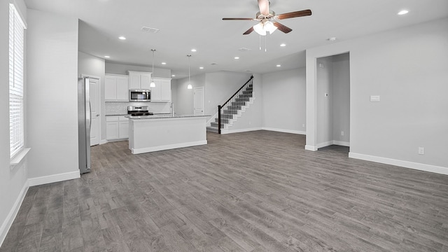 kitchen with appliances with stainless steel finishes, hardwood / wood-style floors, white cabinetry, a kitchen island with sink, and ceiling fan