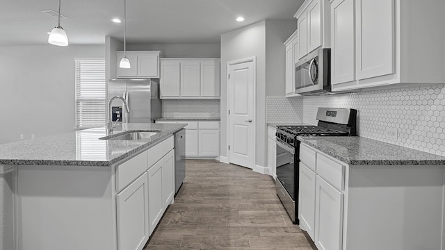 kitchen with backsplash, stainless steel appliances, decorative light fixtures, white cabinetry, and light hardwood / wood-style flooring