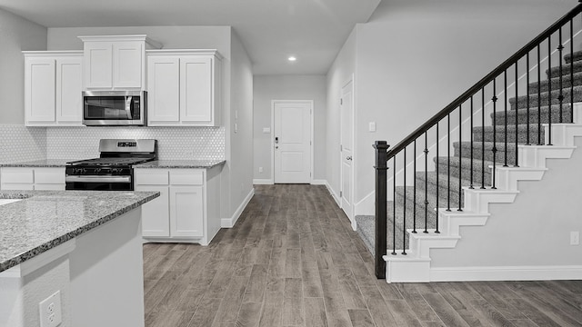 kitchen featuring light hardwood / wood-style flooring, backsplash, white cabinets, light stone counters, and stainless steel appliances