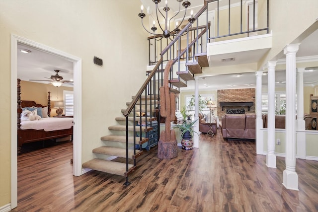 stairway featuring hardwood / wood-style floors, ornamental molding, decorative columns, a fireplace, and ceiling fan with notable chandelier