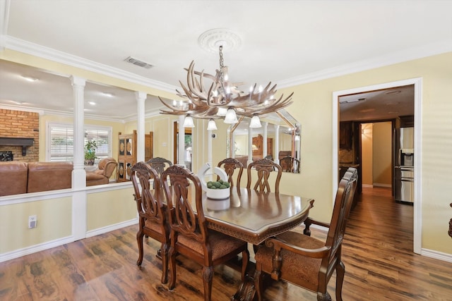 dining room with dark hardwood / wood-style floors, a chandelier, brick wall, ornamental molding, and ornate columns