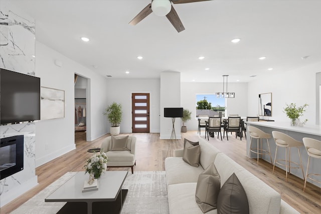 living room with ceiling fan with notable chandelier and light wood-type flooring