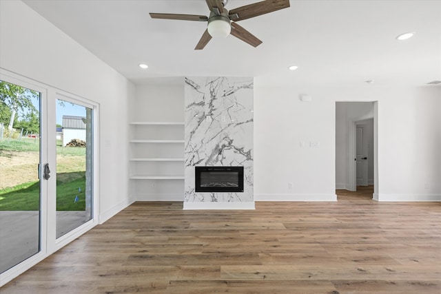 unfurnished living room featuring wood-type flooring, built in shelves, ceiling fan, and a premium fireplace