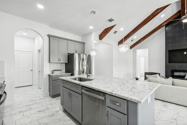 kitchen featuring vaulted ceiling with beams, gray cabinets, a kitchen island with sink, and appliances with stainless steel finishes