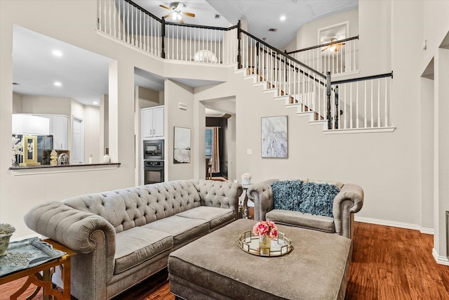 living room with ceiling fan, hardwood / wood-style flooring, and a towering ceiling