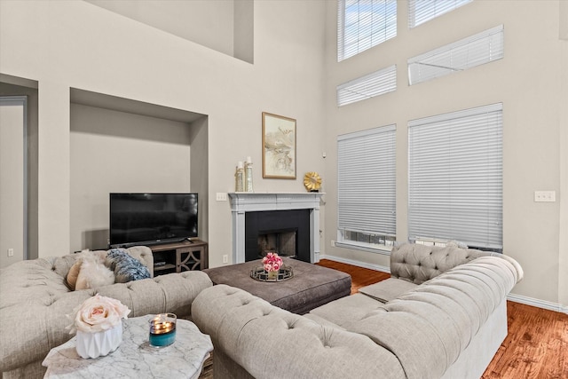 living area with a towering ceiling, a fireplace, baseboards, and wood finished floors