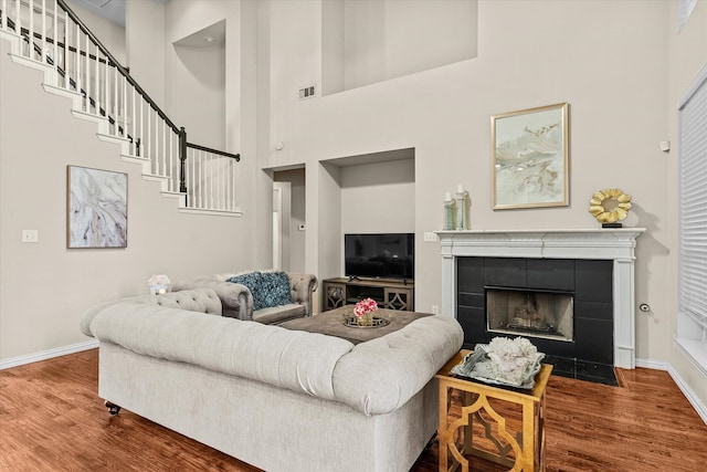 living room featuring a towering ceiling, hardwood / wood-style floors, and a tile fireplace