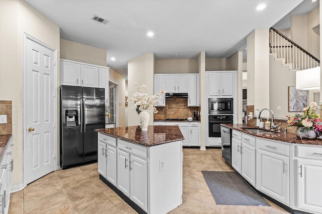 kitchen featuring decorative backsplash, sink, black appliances, white cabinets, and a center island