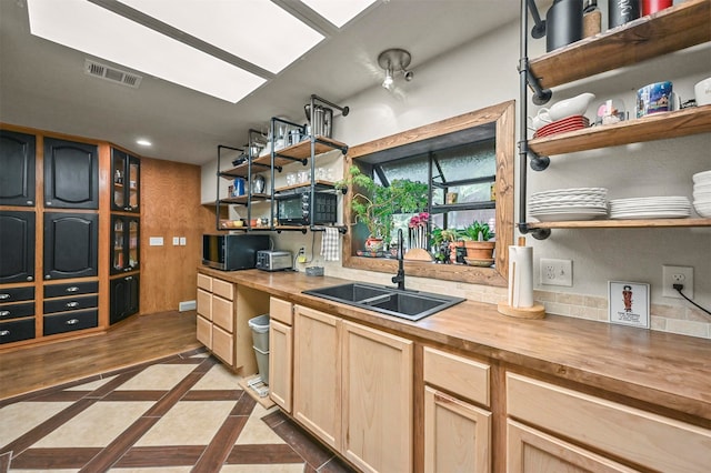 kitchen featuring light brown cabinets, butcher block countertops, a skylight, light tile patterned floors, and sink