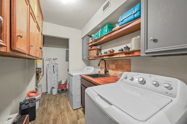 clothes washing area featuring light wood-type flooring, washing machine and dryer, sink, and cabinets