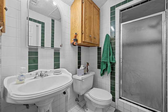 bathroom featuring a shower with door, sink, toilet, tile walls, and a textured ceiling