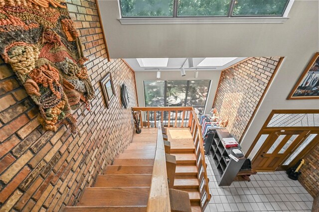 stairway featuring a high ceiling, brick wall, a skylight, and tile patterned floors