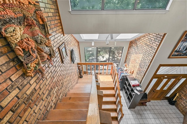 staircase with a wealth of natural light, a skylight, tile patterned flooring, and brick wall