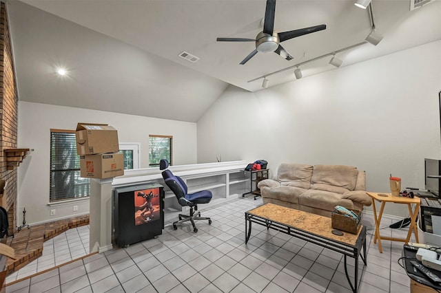 interior space with rail lighting, vaulted ceiling, brick wall, ceiling fan, and a brick fireplace