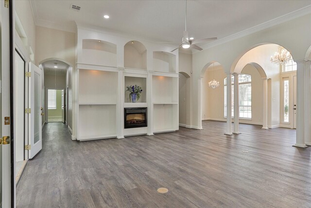 unfurnished living room featuring ornamental molding, built in features, decorative columns, ceiling fan with notable chandelier, and hardwood / wood-style flooring