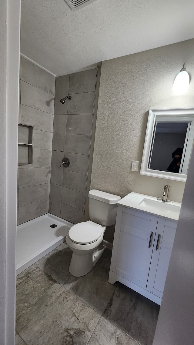 bathroom featuring a tile shower, a textured ceiling, tile patterned flooring, vanity, and toilet