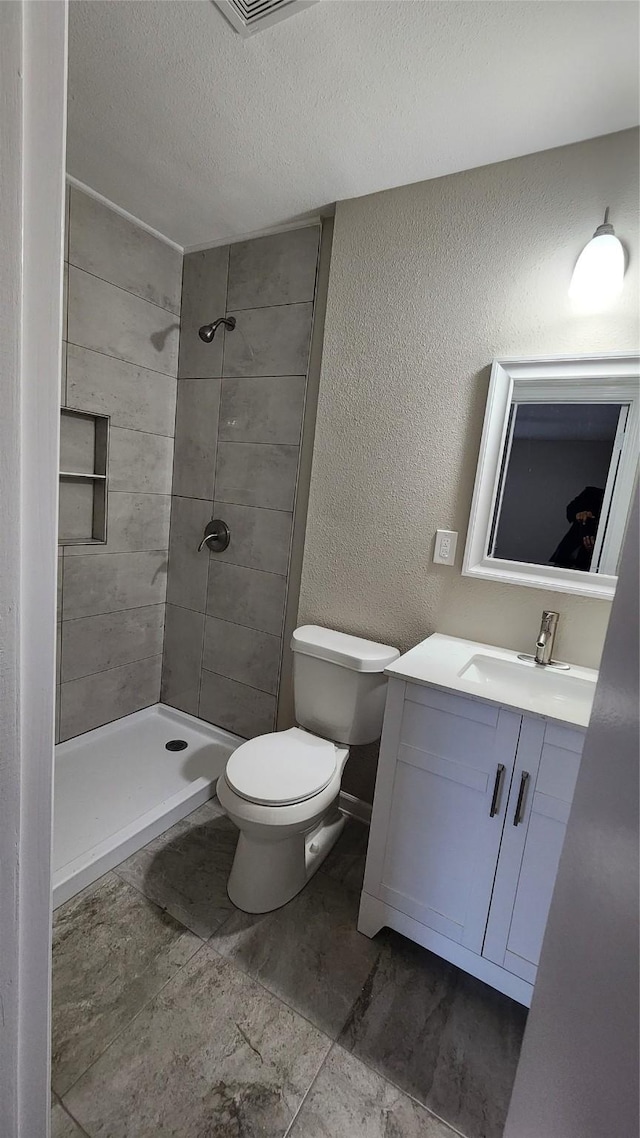 bathroom featuring vanity, tiled shower, a textured ceiling, and toilet