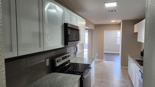 kitchen featuring stainless steel appliances, light tile patterned flooring, white cabinetry, and plenty of natural light