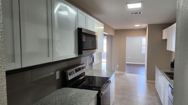 kitchen featuring light tile patterned flooring, white cabinetry, backsplash, light stone counters, and stainless steel appliances