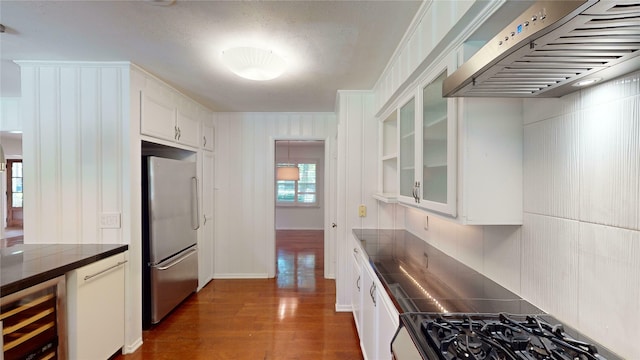 kitchen featuring decorative backsplash, dark hardwood / wood-style flooring, stainless steel refrigerator, white cabinetry, and exhaust hood