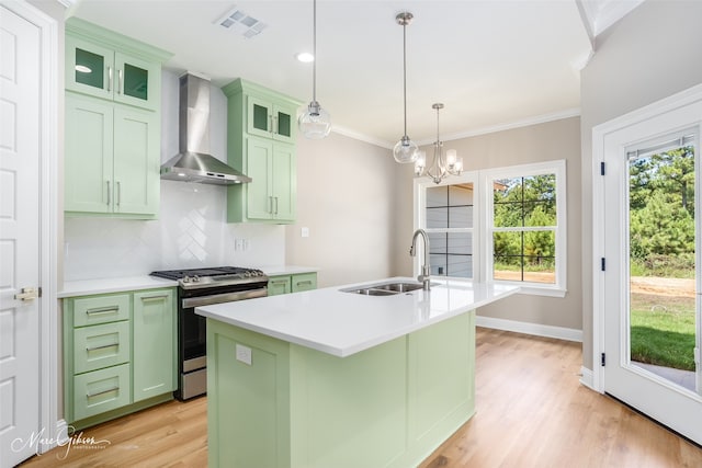 kitchen featuring wall chimney range hood, light wood-type flooring, a kitchen island with sink, stainless steel gas range, and sink