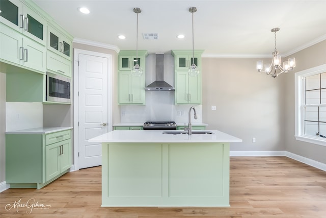 kitchen with wall chimney range hood, tasteful backsplash, a kitchen island with sink, light hardwood / wood-style floors, and stainless steel microwave