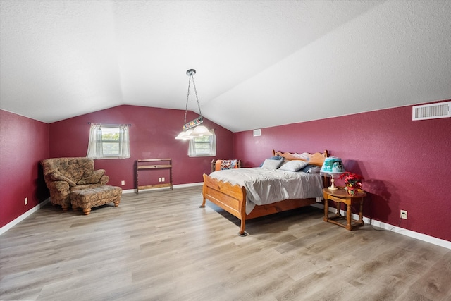 bedroom featuring a textured ceiling, light wood-type flooring, and vaulted ceiling