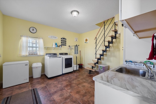 clothes washing area with a textured ceiling, sink, and washing machine and clothes dryer