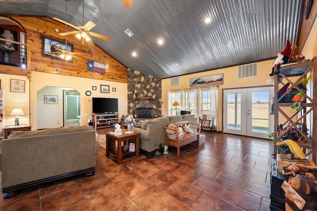 living room with ceiling fan, french doors, wooden walls, high vaulted ceiling, and a fireplace