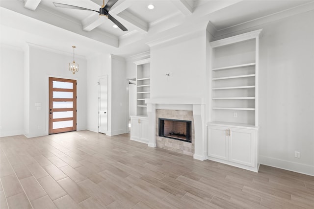 unfurnished living room with coffered ceiling, crown molding, ceiling fan with notable chandelier, a tile fireplace, and beamed ceiling