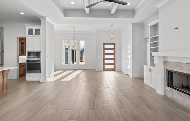 unfurnished living room featuring ceiling fan with notable chandelier, built in features, ornamental molding, a tile fireplace, and beam ceiling