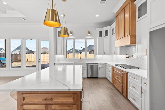 kitchen with white cabinetry, appliances with stainless steel finishes, light stone countertops, a kitchen island, and crown molding