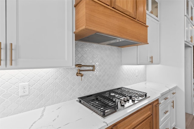 kitchen featuring backsplash, light stone counters, premium range hood, and white cabinetry