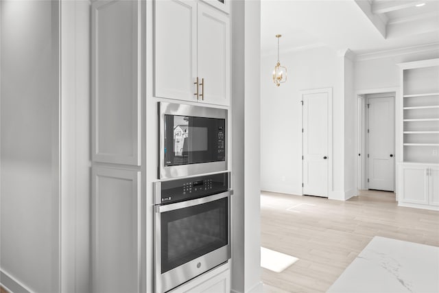 kitchen featuring white cabinetry, stainless steel oven, built in microwave, and decorative light fixtures