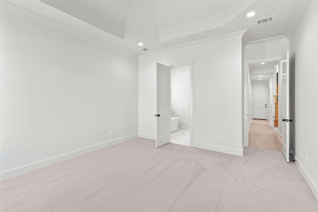 unfurnished bedroom featuring ensuite bathroom, light colored carpet, a tray ceiling, and ornamental molding