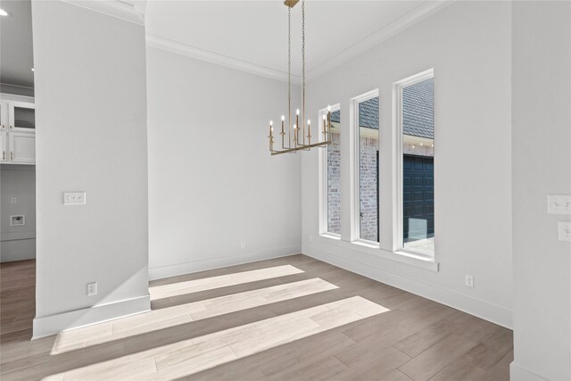 unfurnished dining area featuring a chandelier, crown molding, and hardwood / wood-style floors