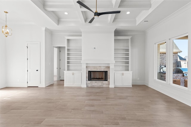 unfurnished living room with ceiling fan with notable chandelier, beamed ceiling, ornamental molding, a tiled fireplace, and coffered ceiling