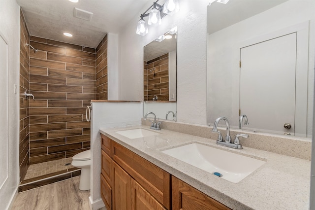 bathroom with hardwood / wood-style flooring, double vanity, a tile shower, and toilet