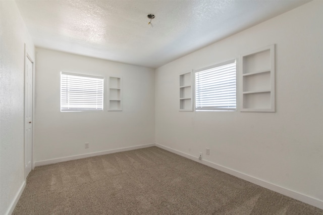 carpeted spare room with a wealth of natural light, built in features, and a textured ceiling