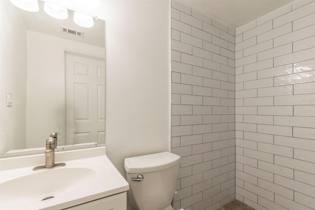 full bathroom with visible vents, vanity, toilet, and tiled shower