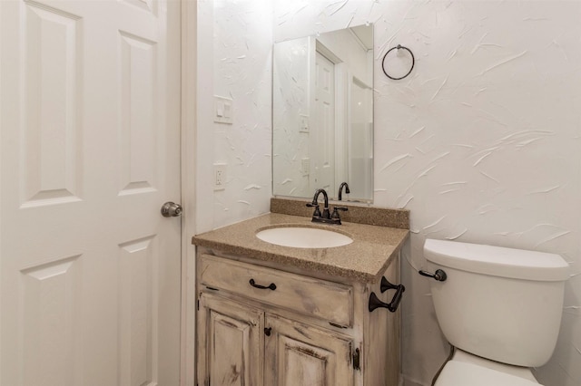 half bath featuring a textured wall, vanity, and toilet