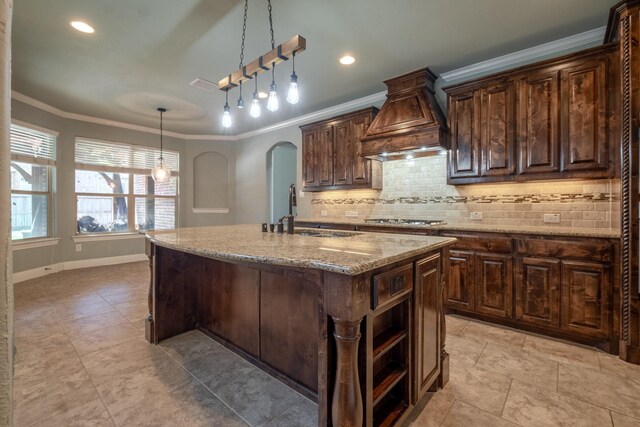 kitchen with sink, light stone countertops, a kitchen island with sink, premium range hood, and light tile patterned floors