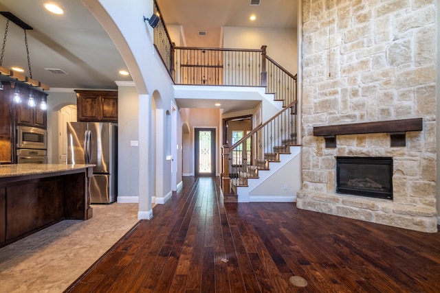 foyer entrance with crown molding, hardwood / wood-style floors, a stone fireplace, and a towering ceiling