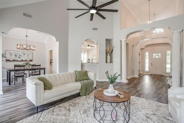 living room with a towering ceiling, ceiling fan with notable chandelier, crown molding, dark hardwood / wood-style flooring, and ornate columns